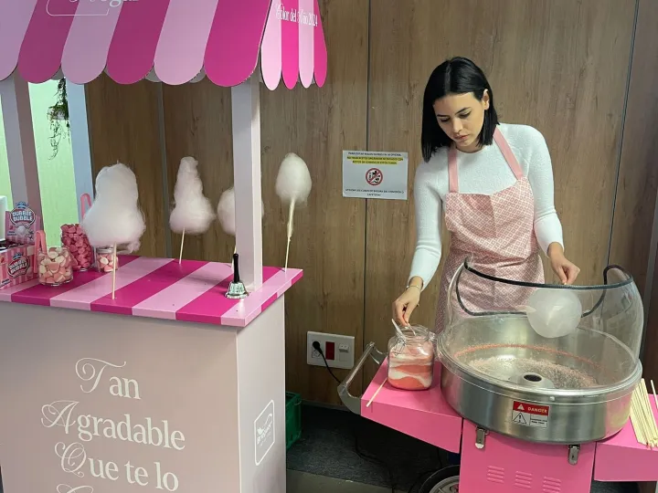 Puesto de algodón de azúcar con toldo rosa y operaria sirviendo