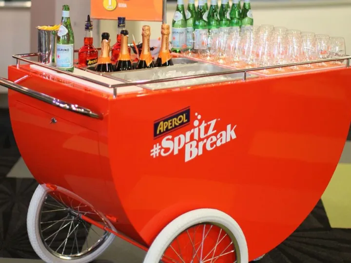 Carrito de spritz rojo con botellas y copas en un evento de interior