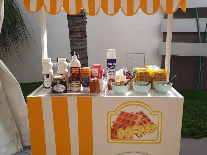 Carrito de gofres con toldo de rayas naranjas y toppings preparados