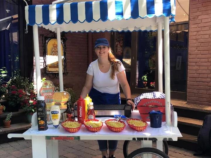 Carrito de hamburguesas con toldo de rayas azules y salsas listas para servir