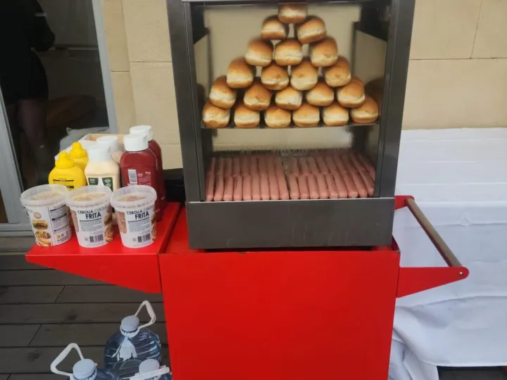 Carrito de hot dog rojo con panecillos y salchichas en la vitrina y salsas a un lado