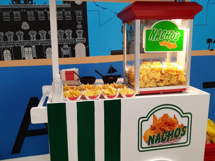 Carrito de nachos con toldo de rayas verdes y blancas y máquina llena de nachos