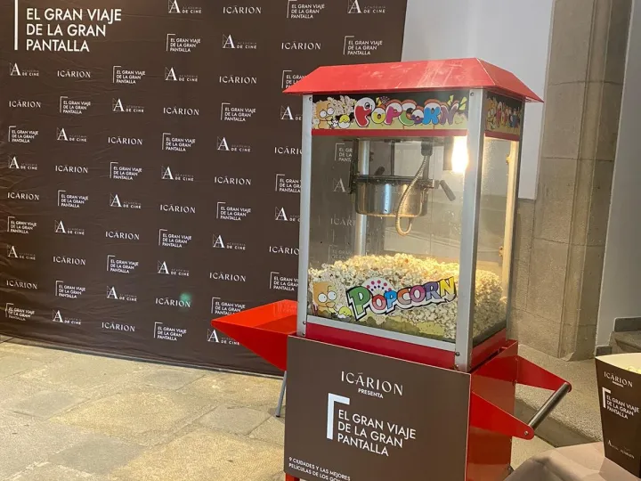 Carrito de palomitas rojo lleno de palomitas, con panel personalizado, en la entrada de un evento de cine