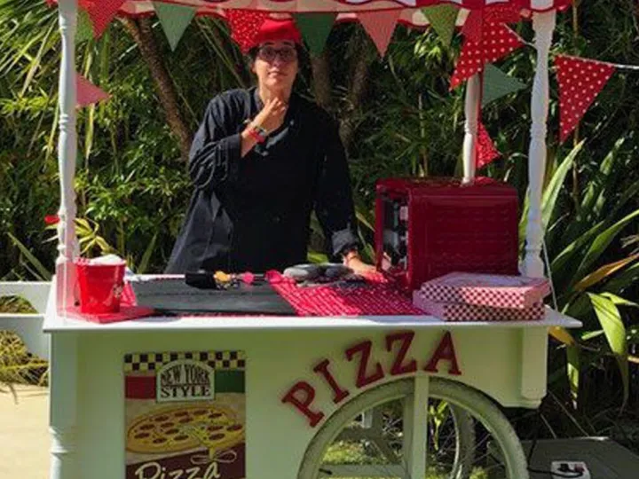 Carrito de pizzas con toldo de rayas rojas y blancas en un jardín