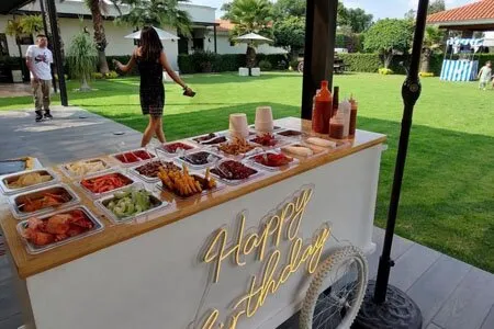 Carrito de charcutería con bandejas de embutidos y quesos en un jardín