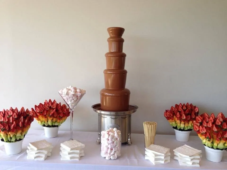 Fuente de chocolate rodeada de brochetas de fresas y nubes