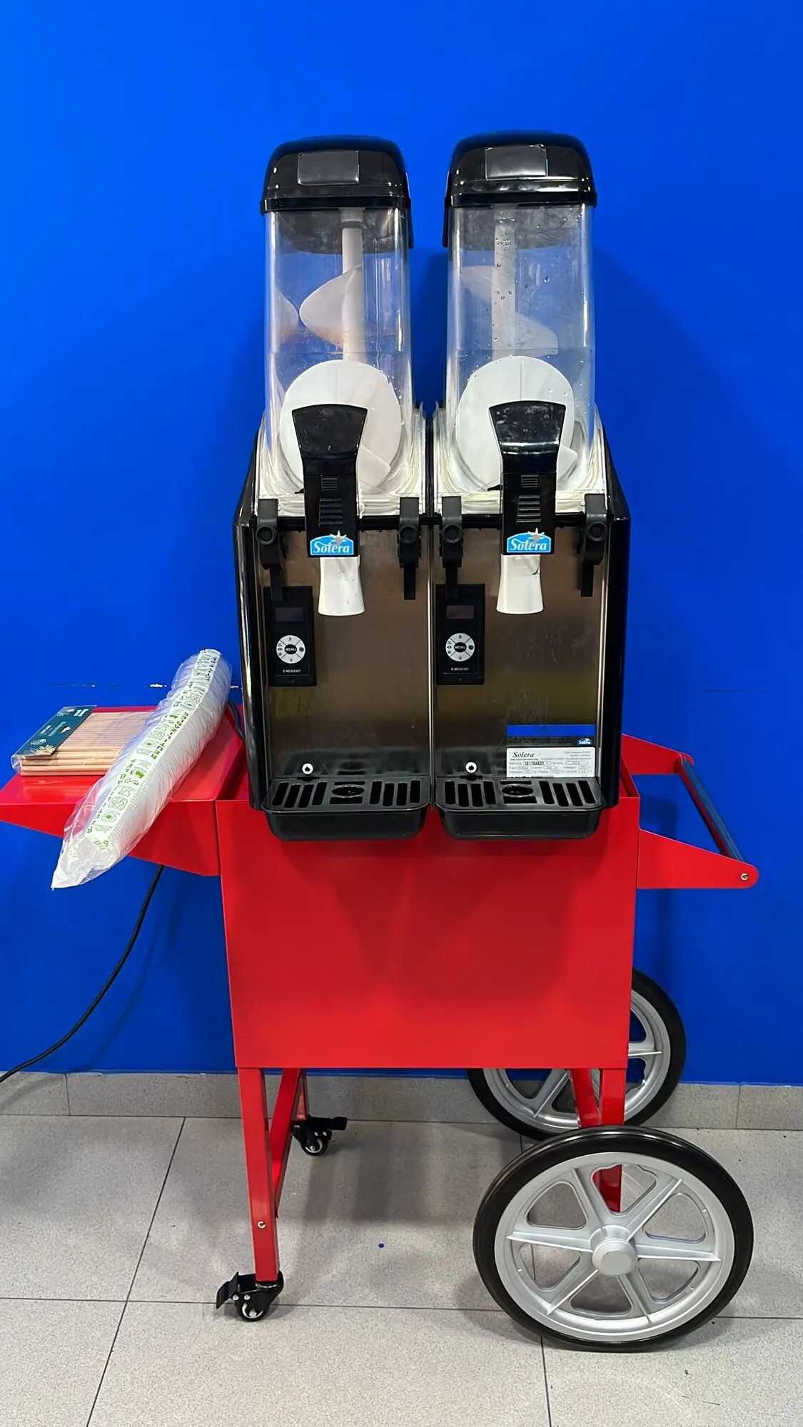 Máquina de granizados de dos cubas sobre carrito rojo con vasos y pajitas