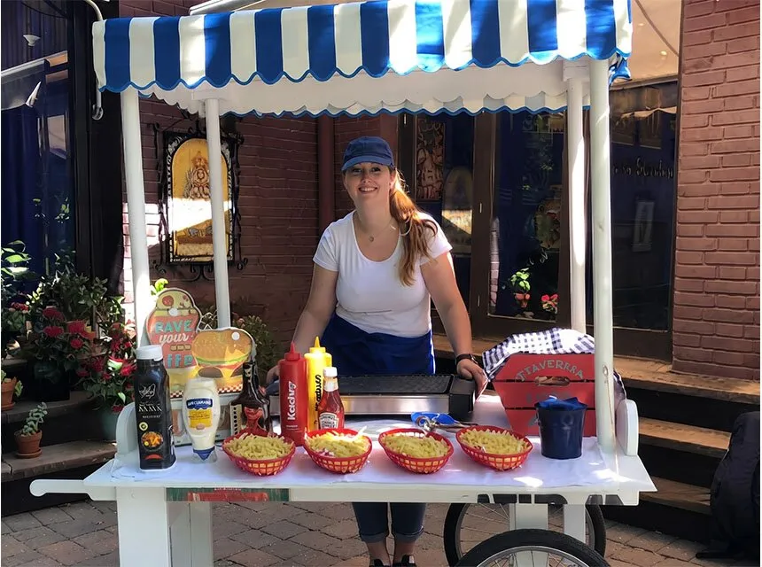 Carrito de hamburguesas con toldo de rayas azules y salsas listas para servir
