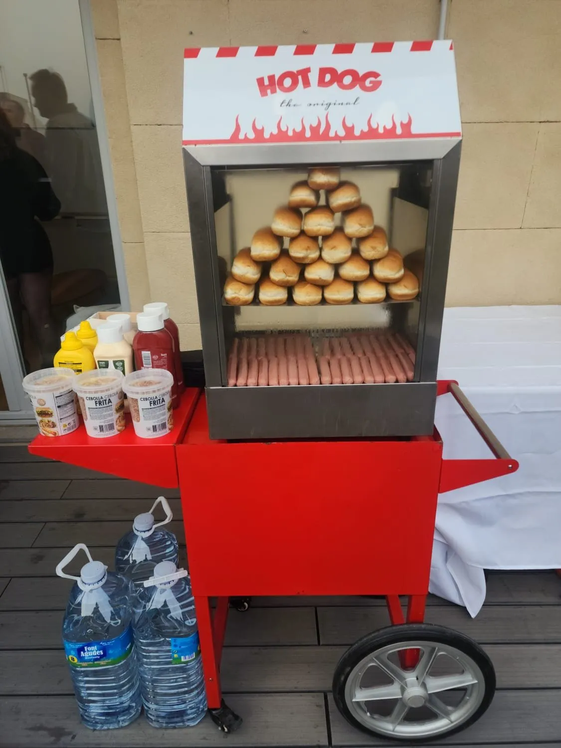 Carrito de hot dog rojo con panecillos y salchichas en la vitrina y salsas a un lado