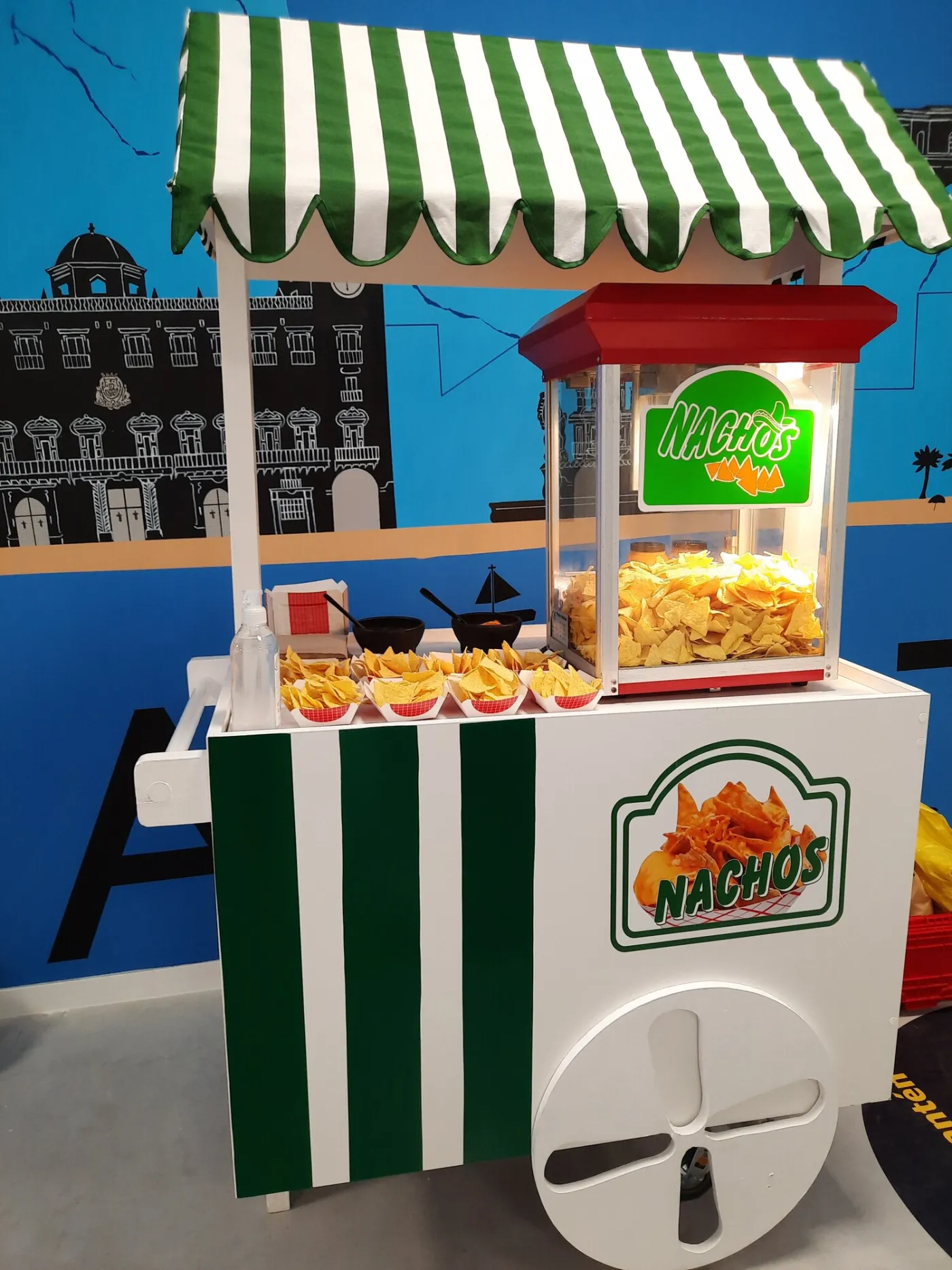 Carrito de nachos con toldo de rayas verdes y blancas y máquina llena de nachos